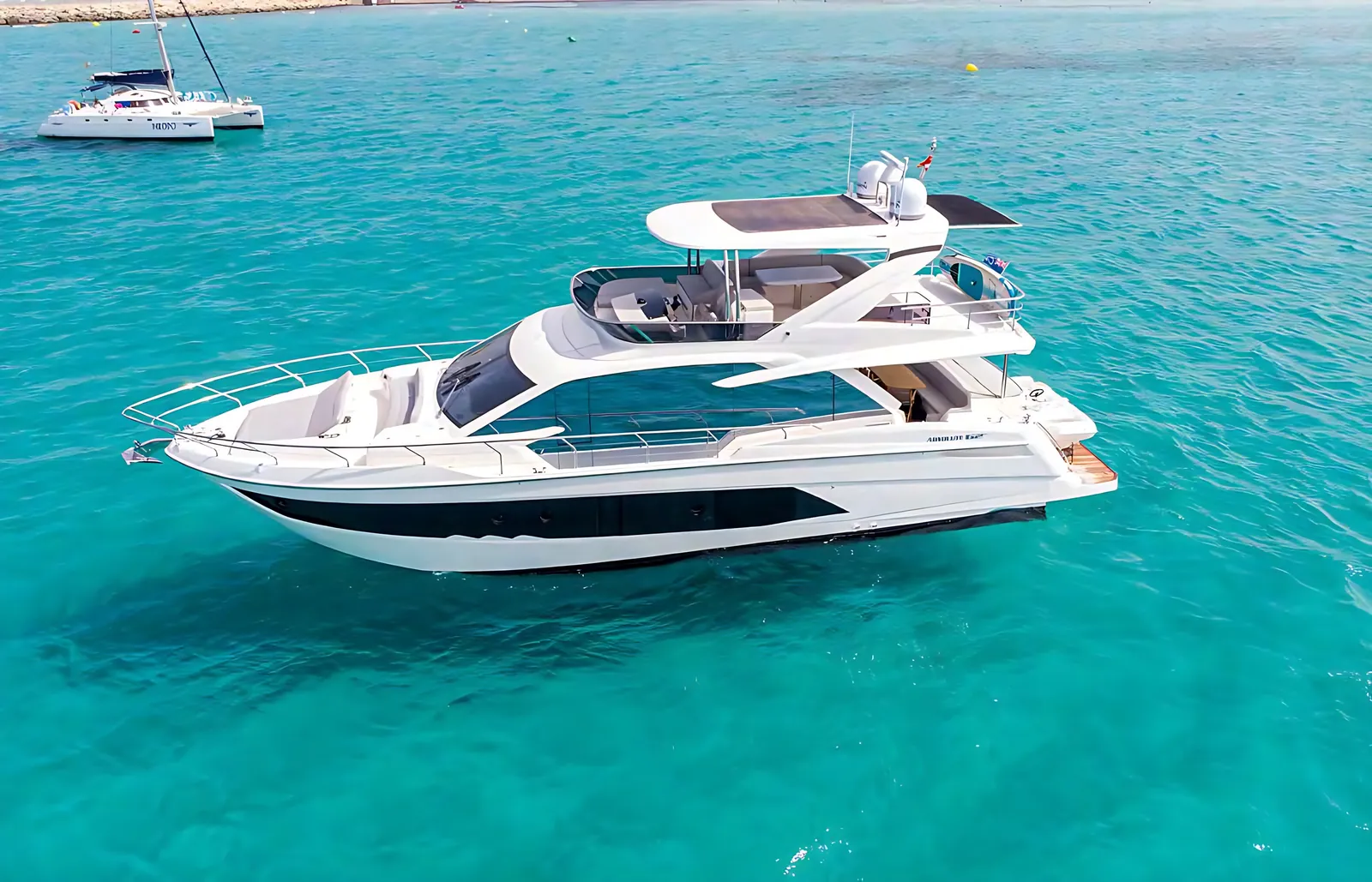 Absolute 62 at anchor in turquoise water, aerial side view of her white hull, flybridge and long dark hull windows