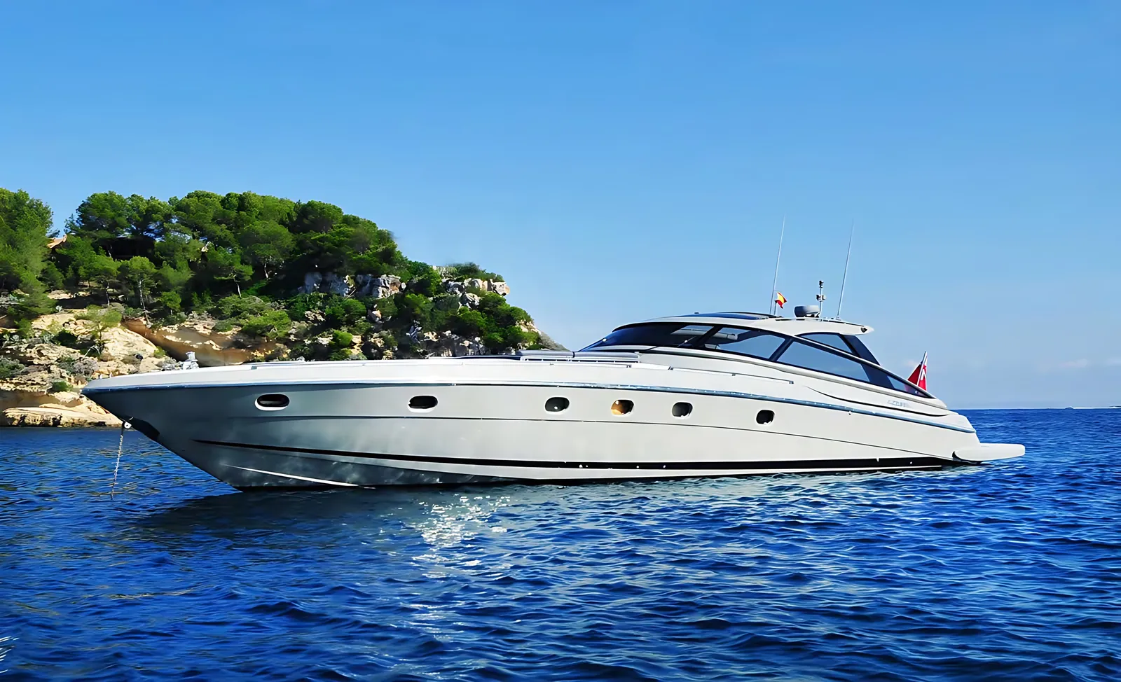 Baia Azzurra 63 open sport yacht at anchor off a pine-covered rocky headland in deep blue water