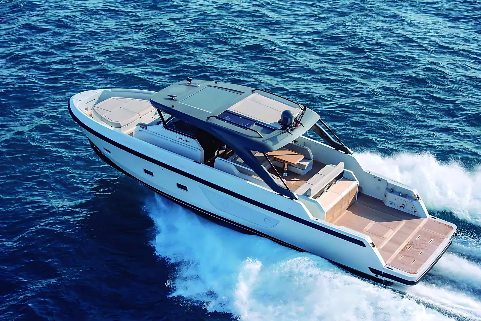 Bluegame 54 running at speed in open water, aerial view of her hardtop, teak aft deck and white wake