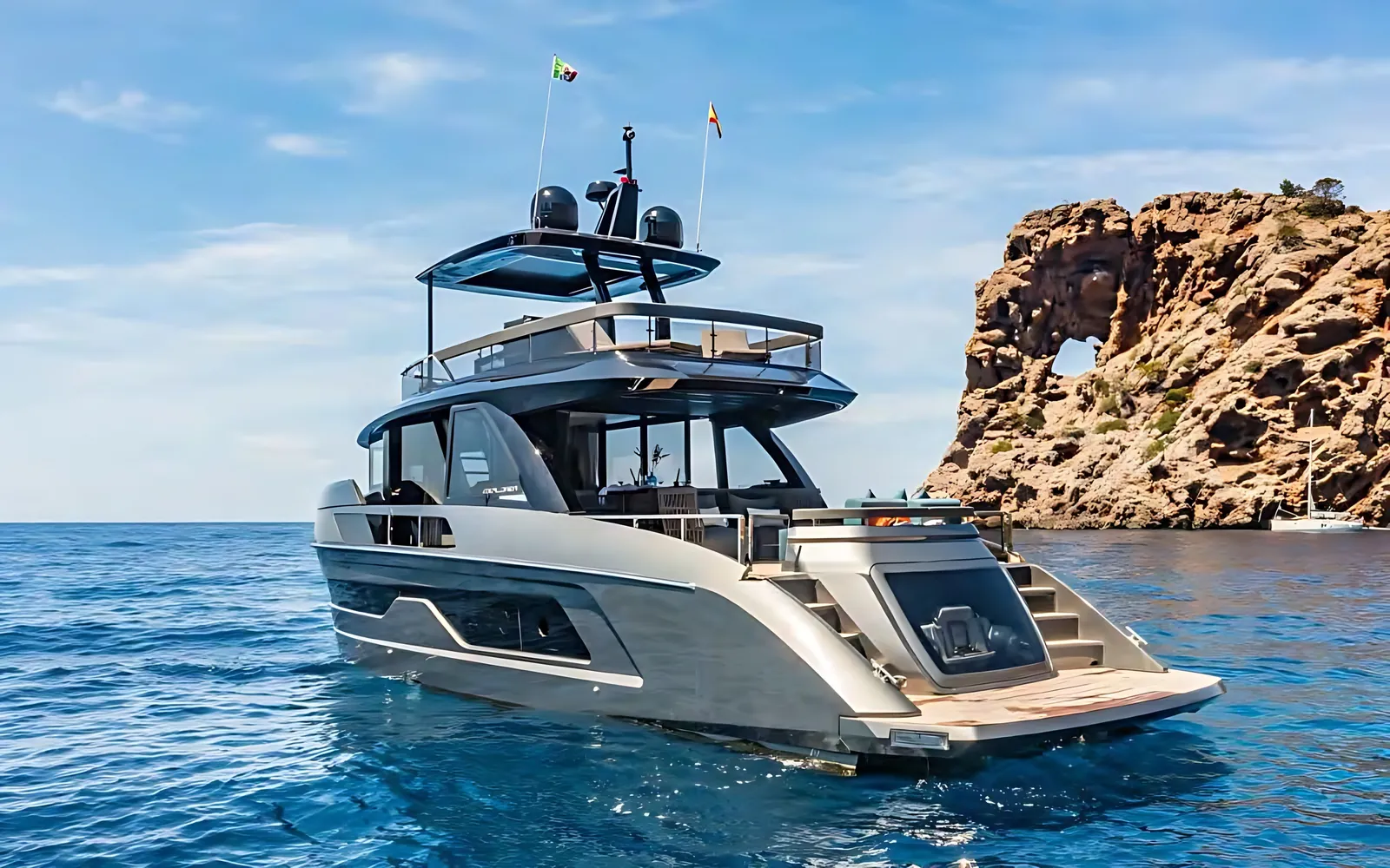 Explorer 62 at rest beside a rocky headland with a natural arch, stern view of her grey hull and glass garage
