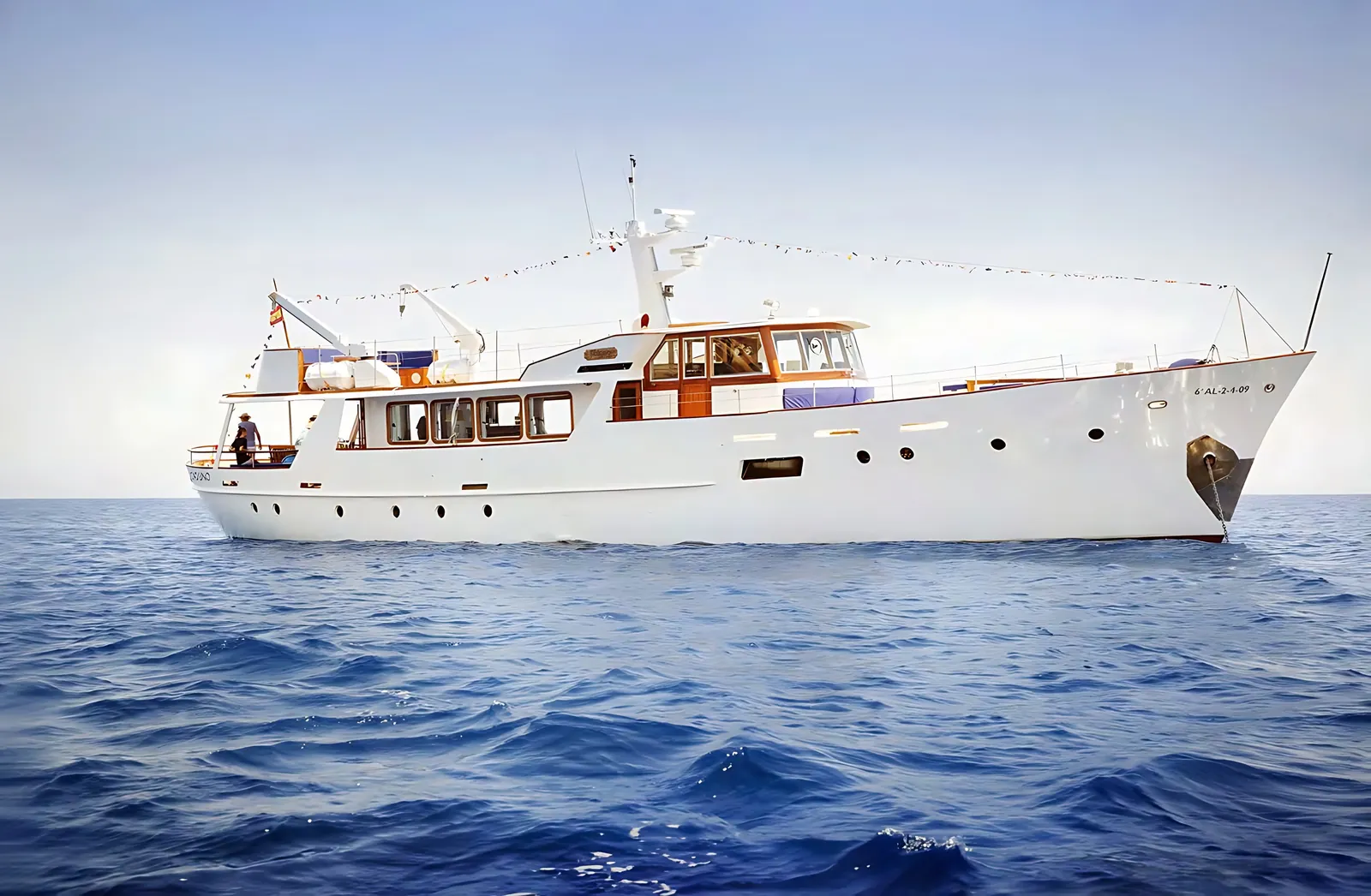 The Feadship classic motor yacht at anchor on open blue water, dressed overall in signal flags