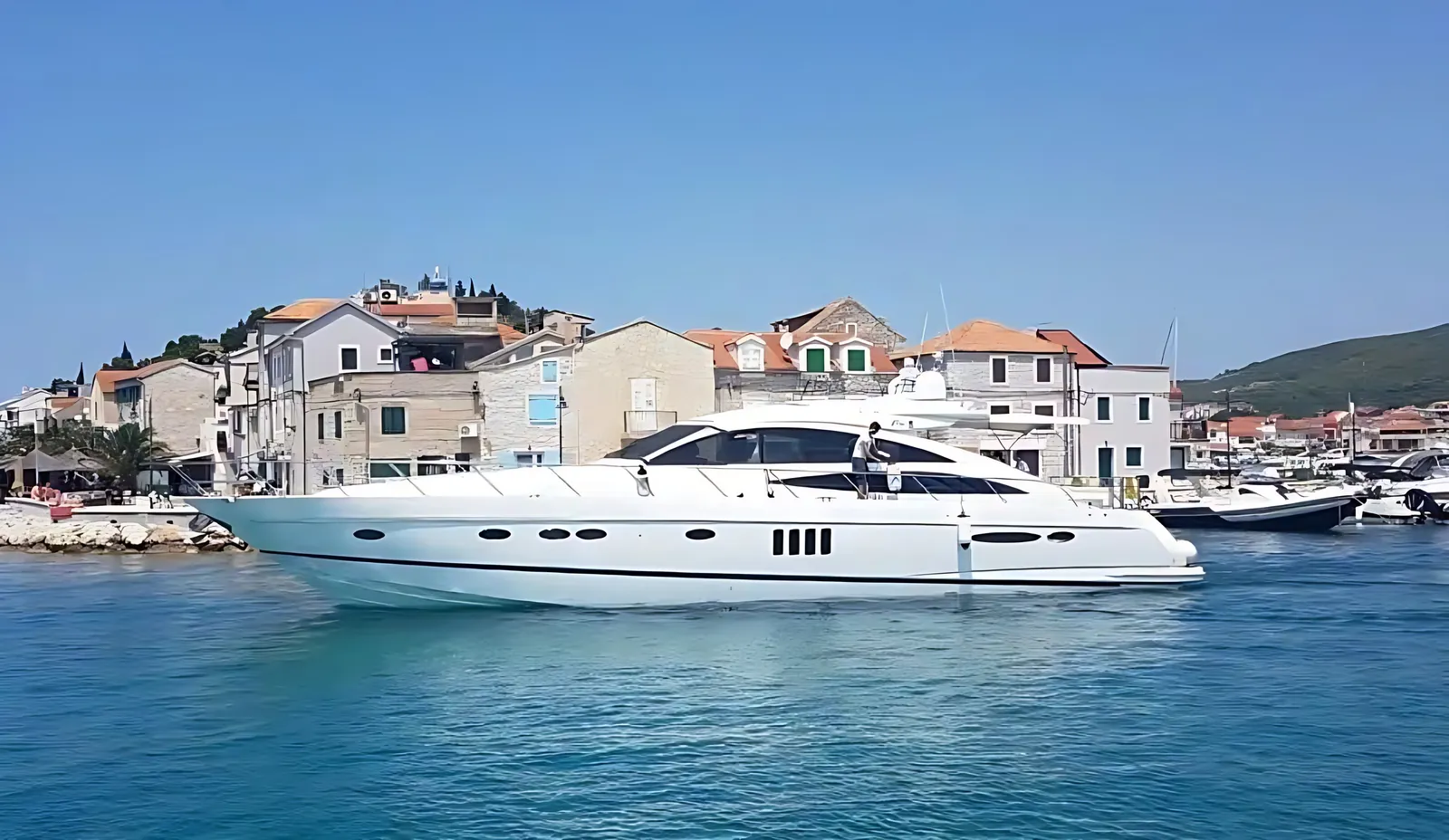 Princess V70 sports yacht moving slowly past a stone harbour town with terracotta roofs