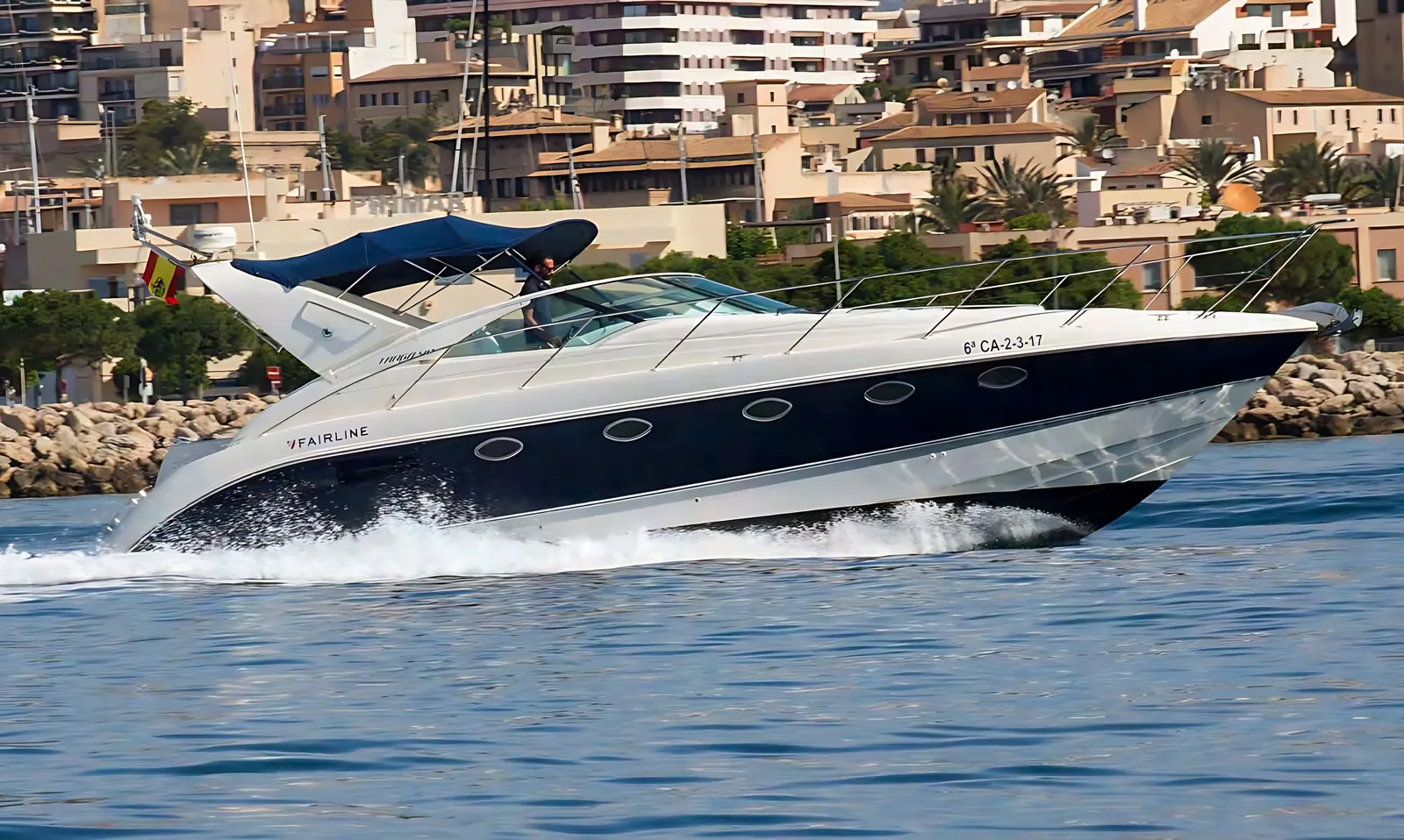 Targa 40 sports cruiser running at speed under a blue bimini, her navy hull throwing spray beside a breakwater