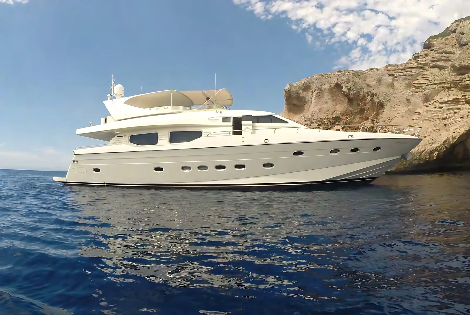 Technema 85 at anchor beside a limestone cliff in clear blue water, her flybridge under a white bimini