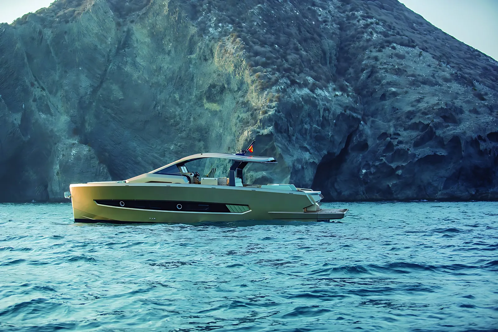 Tesoro 50 at rest on open water beneath a tall rocky headland, side view of her bronze hull and long T-top